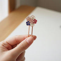 Hand holding a decorative book marker clip with floral designs on a neutral background