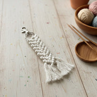 Macrame keychain with tassels on a wooden surface with yarn and knitting needles.