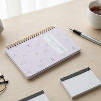 Planner on a desk with a cup of tea, glasses, and a small plant.